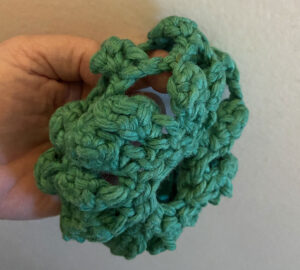 A person holding a green crocheted ball.